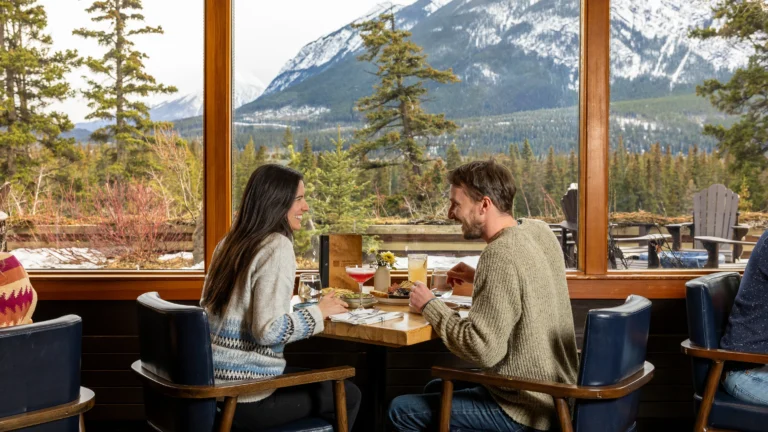 A couple enjoy breakfast at the Juniper Bistro with views over the Bow Valley behind them